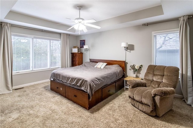 bedroom featuring multiple windows, light carpet, a tray ceiling, and ceiling fan