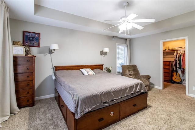 carpeted bedroom with ceiling fan, a raised ceiling, a spacious closet, and a closet