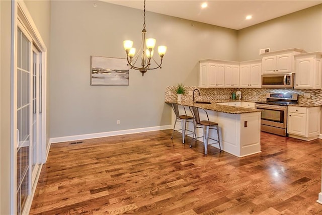 kitchen with white cabinetry, stainless steel appliances, kitchen peninsula, dark stone counters, and decorative light fixtures