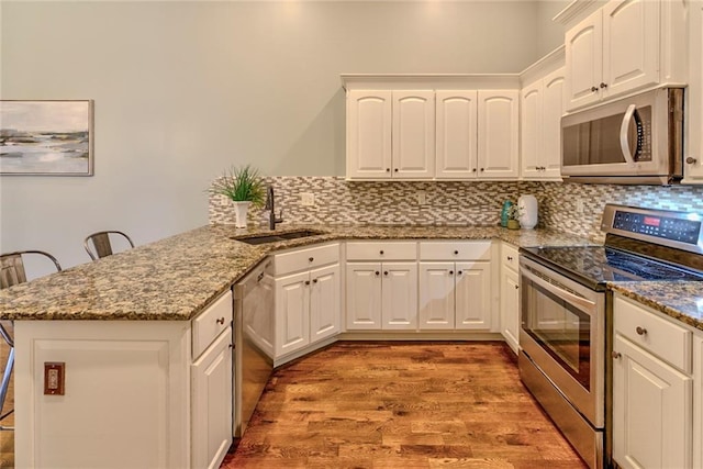 kitchen featuring kitchen peninsula, appliances with stainless steel finishes, a breakfast bar, sink, and white cabinets