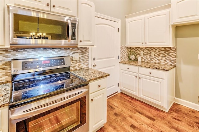 kitchen with dark stone countertops, white cabinetry, light wood-type flooring, and appliances with stainless steel finishes