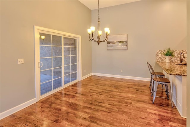 unfurnished dining area featuring sink, hardwood / wood-style floors, and an inviting chandelier