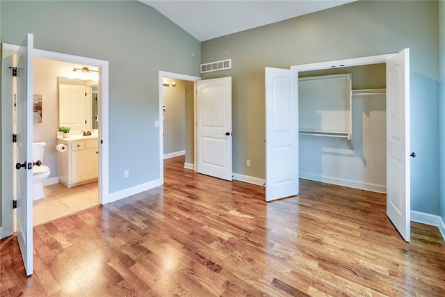 unfurnished bedroom with ensuite bath, a closet, high vaulted ceiling, and light hardwood / wood-style flooring