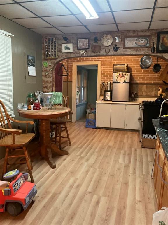 kitchen with light wood-type flooring, a paneled ceiling, and brick wall