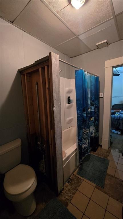 bathroom featuring toilet, shower / tub combo with curtain, a drop ceiling, and tile patterned flooring