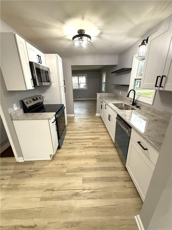 kitchen featuring sink, light wood-type flooring, appliances with stainless steel finishes, light stone counters, and white cabinetry