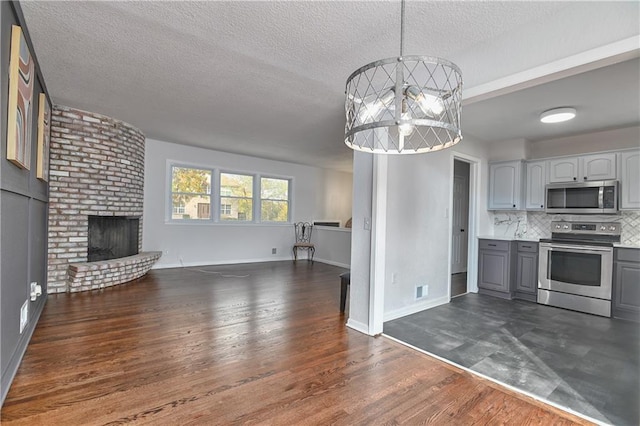 kitchen featuring gray cabinetry, hanging light fixtures, a brick fireplace, decorative backsplash, and stainless steel appliances