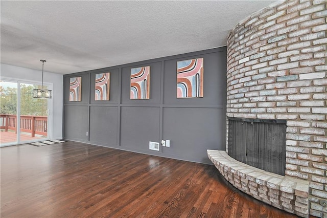 unfurnished living room featuring an inviting chandelier, dark hardwood / wood-style flooring, a textured ceiling, and a brick fireplace