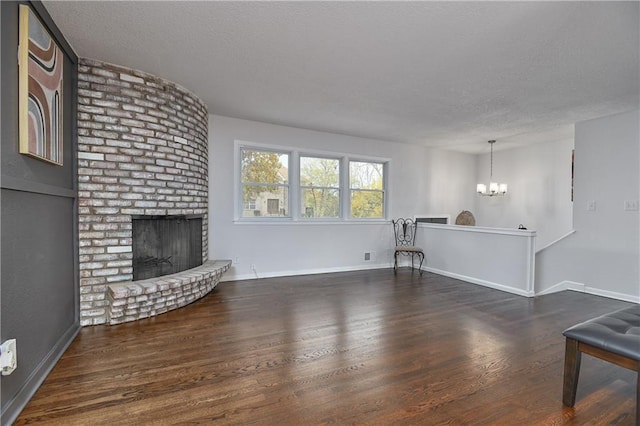 living room featuring a chandelier, a textured ceiling, dark hardwood / wood-style flooring, and a brick fireplace