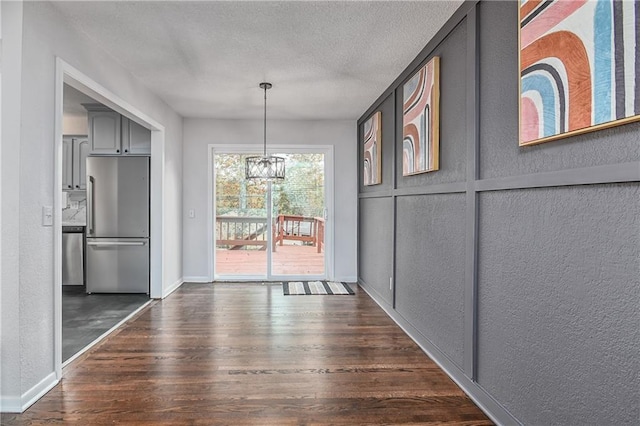 unfurnished dining area with a textured ceiling, dark wood-type flooring, and a chandelier