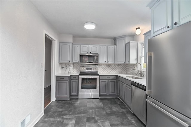 kitchen featuring stainless steel appliances, gray cabinets, tasteful backsplash, and sink