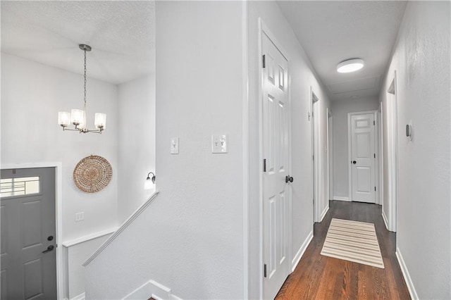 hallway featuring a textured ceiling, a notable chandelier, and dark wood-type flooring