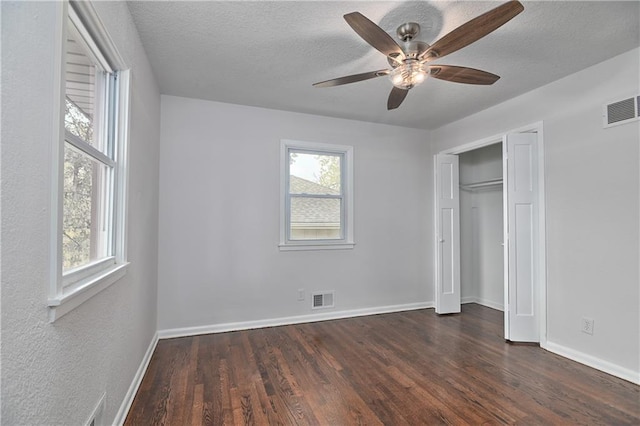 unfurnished bedroom with multiple windows, ceiling fan, dark wood-type flooring, and a textured ceiling