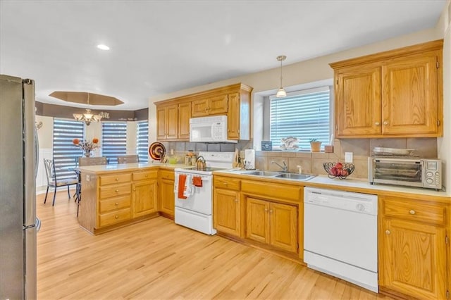 kitchen featuring white appliances, sink, decorative light fixtures, a notable chandelier, and light hardwood / wood-style floors