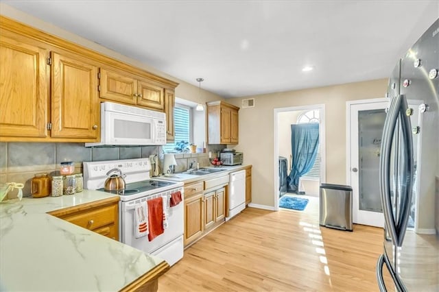 kitchen featuring decorative backsplash, white appliances, sink, light hardwood / wood-style flooring, and hanging light fixtures