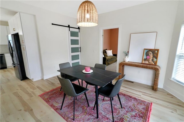 dining room with a barn door and light hardwood / wood-style flooring