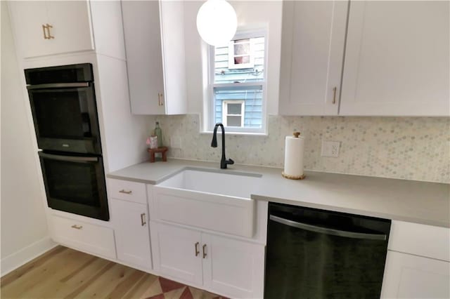 kitchen with a sink, white cabinets, light countertops, backsplash, and black appliances