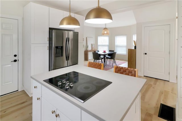 kitchen with light wood finished floors, visible vents, stainless steel fridge with ice dispenser, black electric stovetop, and light countertops