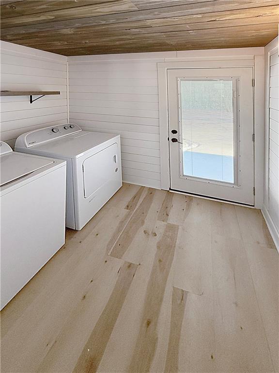 laundry room with laundry area, light wood-style floors, wooden ceiling, independent washer and dryer, and wood walls