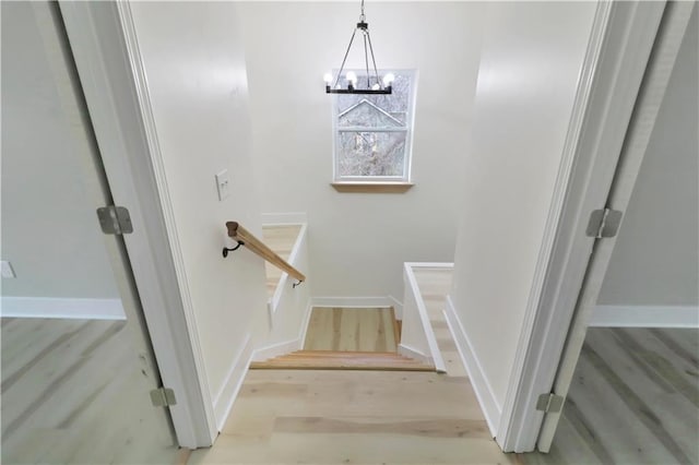 stairway featuring baseboards, a chandelier, and wood finished floors