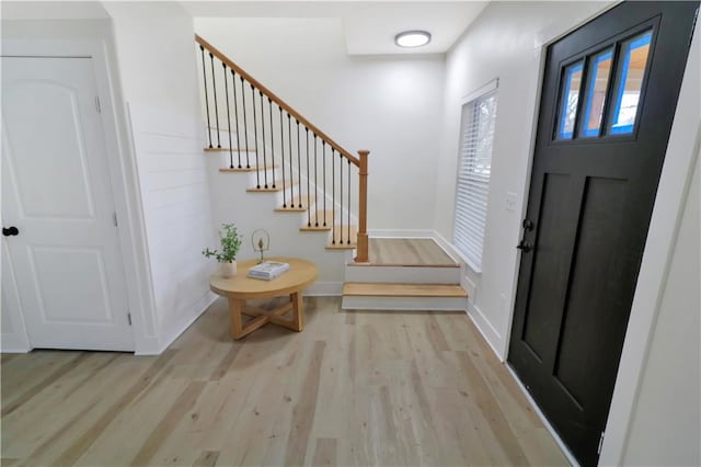 foyer with baseboards, light wood finished floors, and stairs