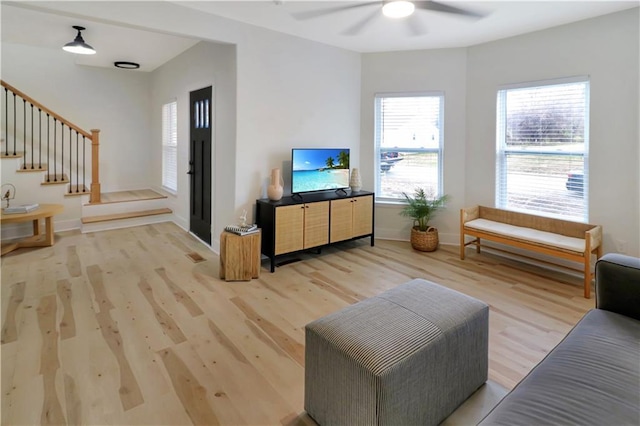 living area featuring light wood-style floors, ceiling fan, stairway, and baseboards