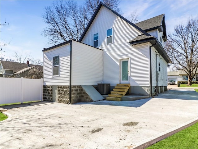 rear view of property featuring entry steps, driveway, a garage, central AC unit, and fence