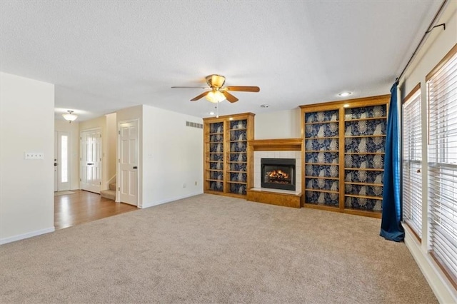 unfurnished living room featuring carpet flooring, ceiling fan, and a tiled fireplace