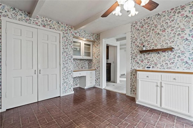 interior space with ceiling fan, white cabinets, and beamed ceiling