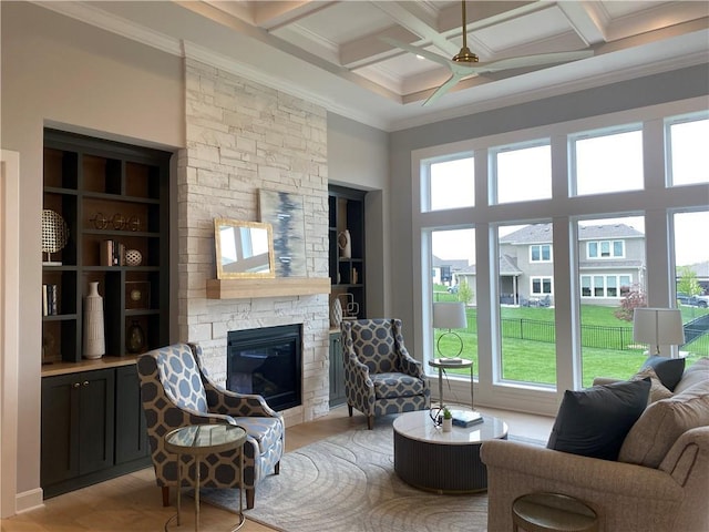 living area with beam ceiling, a wealth of natural light, ornamental molding, and a stone fireplace