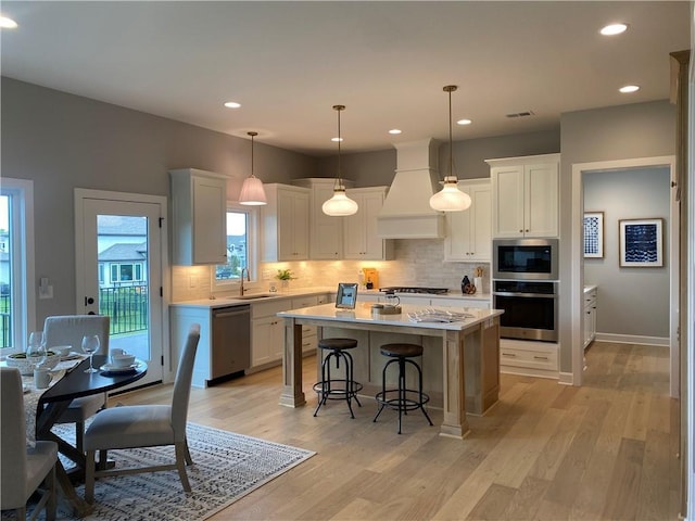 kitchen with a breakfast bar area, custom range hood, a sink, appliances with stainless steel finishes, and light countertops