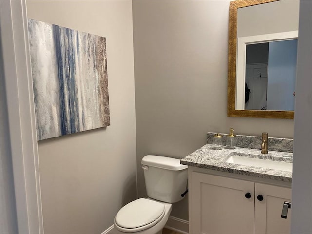 half bathroom with vanity, toilet, and baseboards