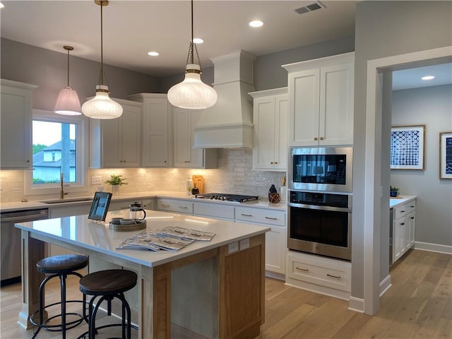 kitchen with stainless steel appliances, light countertops, premium range hood, and a sink