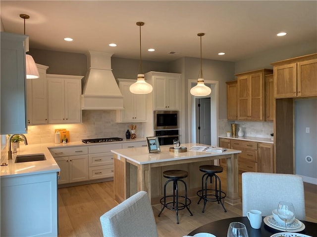 kitchen with custom range hood, backsplash, a sink, light wood-type flooring, and gas cooktop