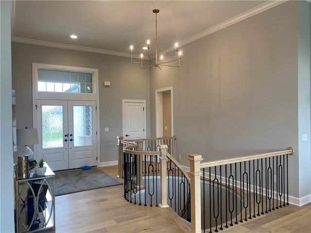 foyer entrance with a chandelier, light wood-style flooring, baseboards, ornamental molding, and french doors