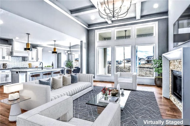 living room featuring a fireplace, coffered ceiling, beamed ceiling, hardwood / wood-style floors, and a chandelier