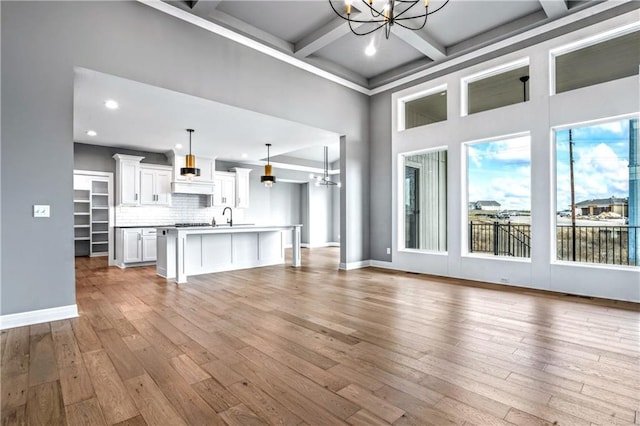 unfurnished living room featuring coffered ceiling, sink, light hardwood / wood-style flooring, an inviting chandelier, and beamed ceiling