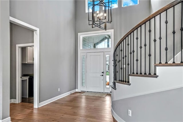 entryway with wood-type flooring, a towering ceiling, and a chandelier