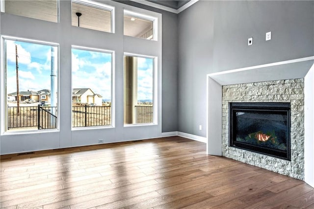 unfurnished living room featuring hardwood / wood-style flooring, a stone fireplace, a wealth of natural light, and ornamental molding