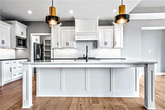 kitchen with a center island with sink, white cabinets, decorative backsplash, built in microwave, and decorative light fixtures