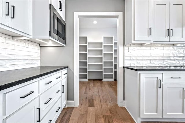 interior space featuring built in microwave, white cabinetry, dark stone countertops, and hardwood / wood-style flooring