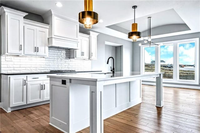 kitchen featuring backsplash, a kitchen island with sink, white cabinets, sink, and decorative light fixtures