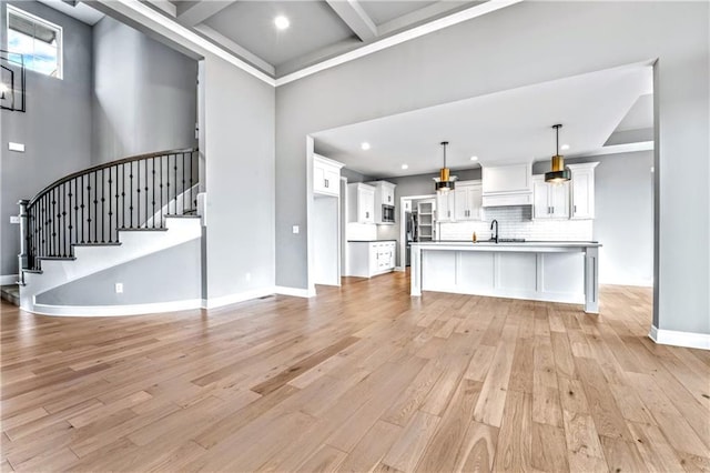 unfurnished living room with beam ceiling, light wood-type flooring, sink, and coffered ceiling