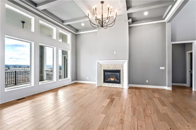 unfurnished living room with light hardwood / wood-style flooring, beamed ceiling, coffered ceiling, and a notable chandelier