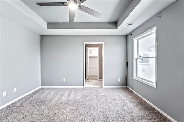 carpeted spare room with a raised ceiling, ceiling fan, and a healthy amount of sunlight