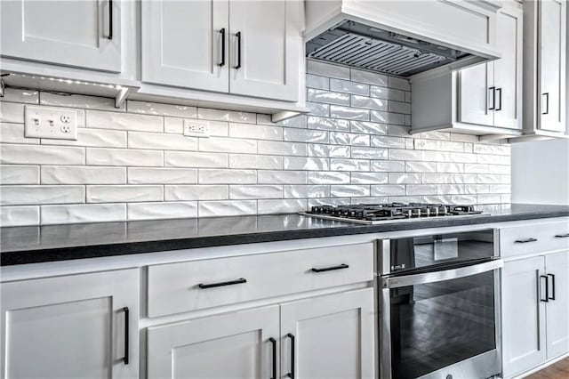 kitchen featuring premium range hood, backsplash, white cabinets, and appliances with stainless steel finishes