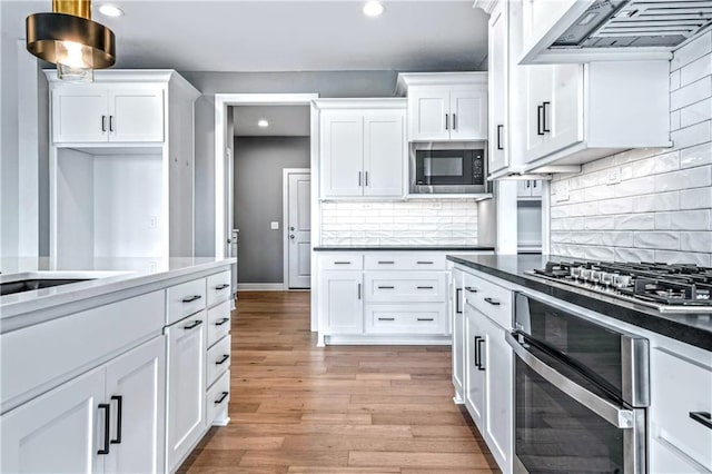 kitchen featuring exhaust hood, white cabinets, light hardwood / wood-style flooring, decorative backsplash, and appliances with stainless steel finishes