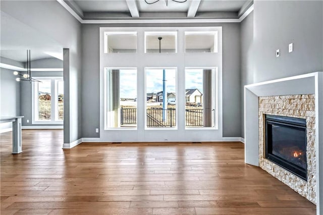 unfurnished living room with coffered ceiling, wood-type flooring, beamed ceiling, a chandelier, and a stone fireplace