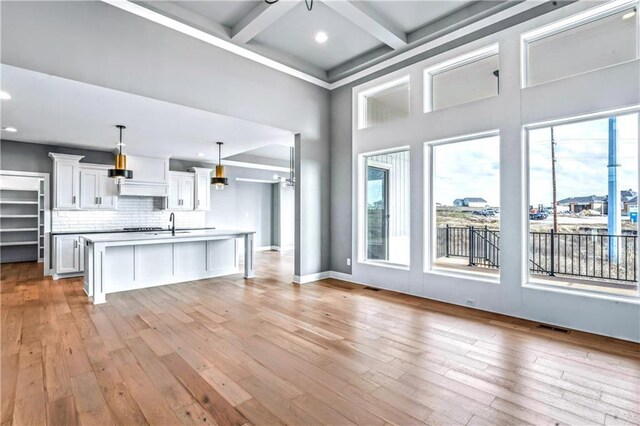 kitchen featuring white cabinetry, coffered ceiling, beamed ceiling, decorative light fixtures, and a kitchen island with sink