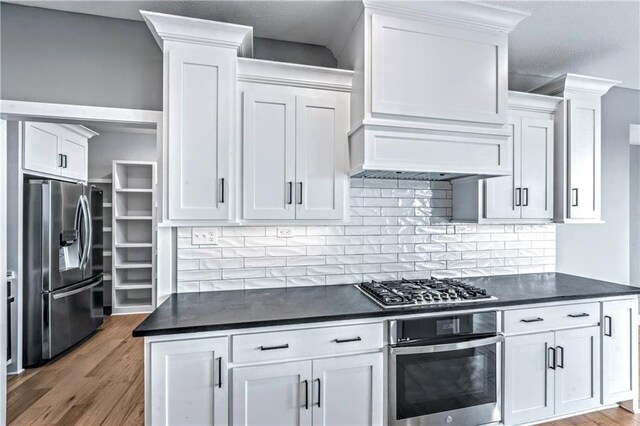 kitchen featuring stainless steel appliances, backsplash, premium range hood, wood-type flooring, and white cabinets